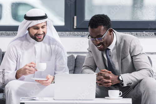 Businessmen looking on laptop and smiling in modern office