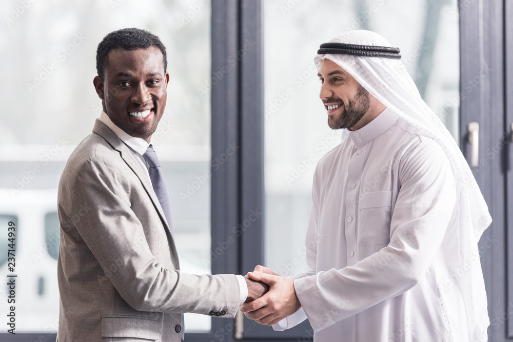 close up view of african american businessman and arabic partner shaking hands in office