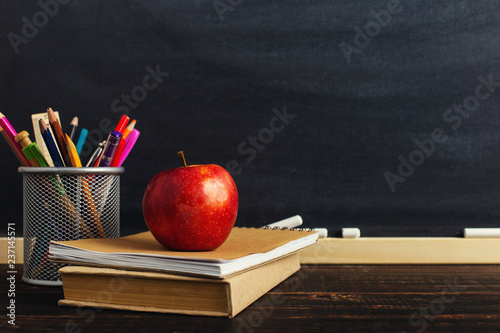 Teacher's desk with writing materials, a book and an apple, a blank for text or a background for a school theme. Copy space.