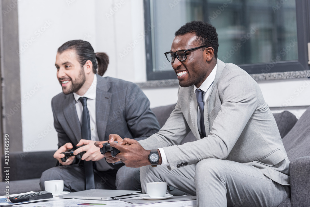 multiethnic businessmen sitting on couch and playing video game with gamepads multiethnic businessmen sitting on couch and playing video game with gamepads