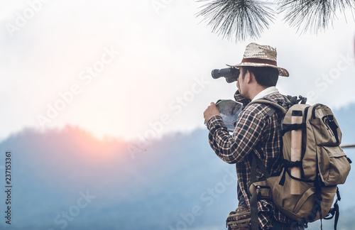 Young hiker with backpack standing looking through binoculars.