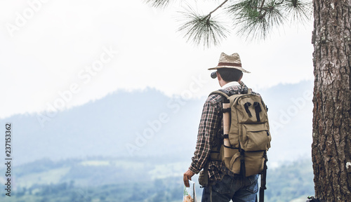 Young hiker with backpack standing looking through binoculars on the mountain