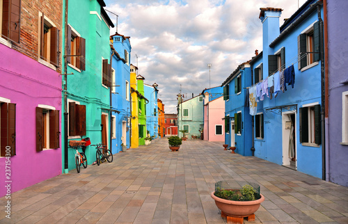 Burano island picturesque street and courtyard with small colorful houses in row against cloudy blue sky, Venice Italy