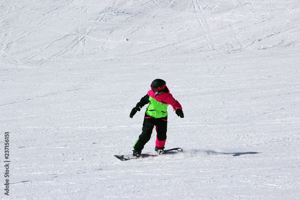 girl in a colorful suit is on a snowboard rides with mountains