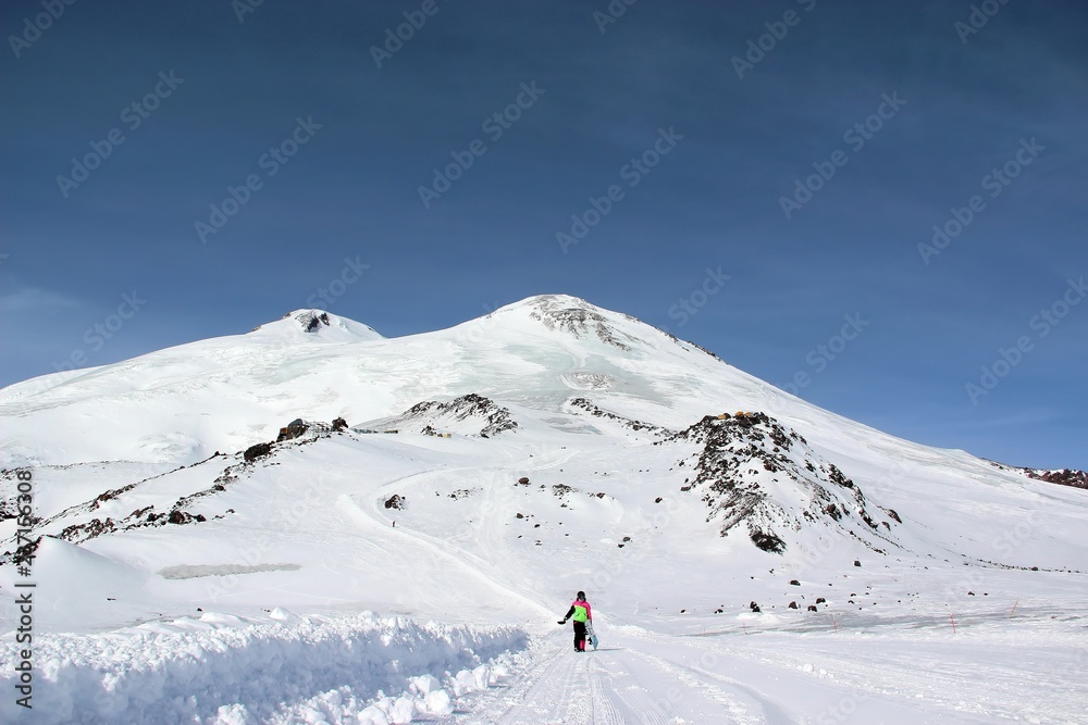 girl in a colorful suit with a snowboard is on the mountain road