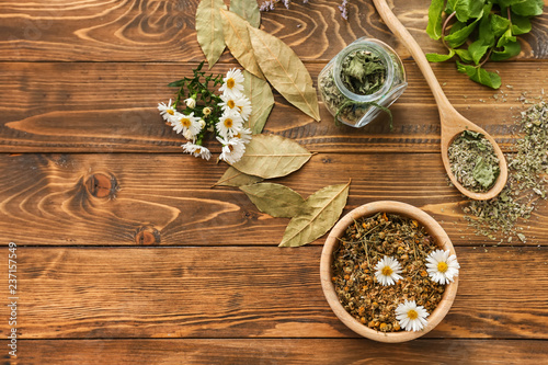 Bowl with dried chamomile flowers and herbs on wooden table