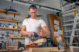 A carpenter works on woodworking the machine tool. Saws furniture details with a circular saw. Process of sawing parts in parts. Against the background of the workshop