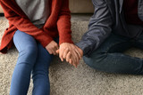 Loving young couple holding hands while sitting on floor at home, closeup
