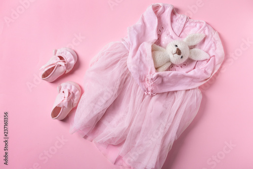 Baby dress, shoes and toy on color background, top view