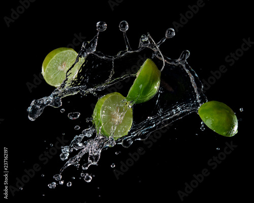 Limes with water splash or explosion flying in the air isolated on black background