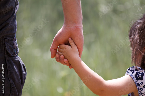 Dad holding his little girl's hand with nature at background.