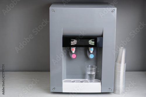 Modern water cooler with plastic cups on white table