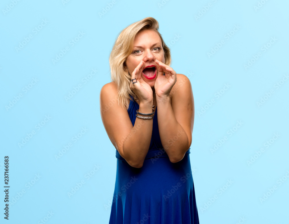 Pregnant blonde woman with blue dress shouting with mouth wide open on isolated blue background Pregnant blonde woman with blue dress shouting with mouth wide open on isolated blue background