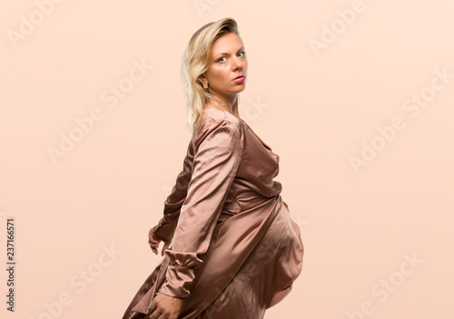 Pregnant blonde woman with elegant dress on occher background