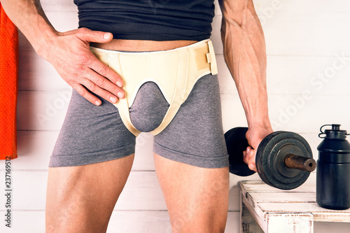 Inguinal hernia belt girding man on workout - Sportive male checks pressure of professional band in pain area of the lower abdomen 