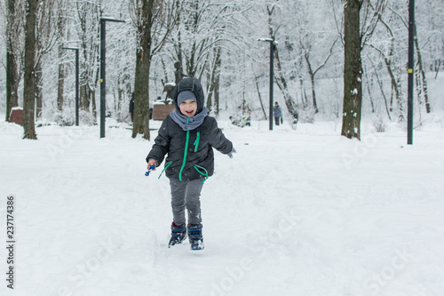 A little boy runs through the snow in the park.