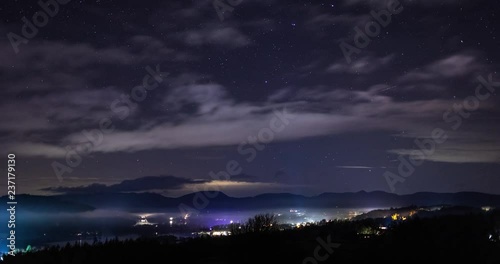 Night sky timelapse over a town with plane lights. Bright lights from town by lake. Bowness on Windermere, UK. 4K 