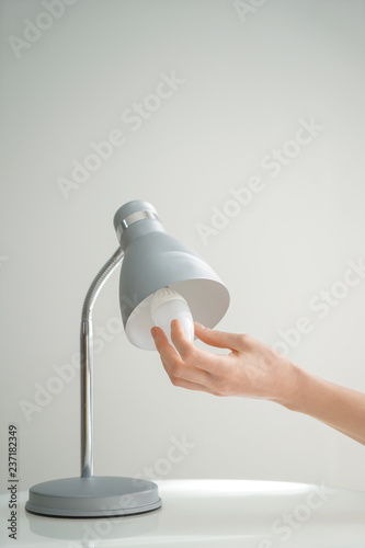 Woman changing light bulb in lamp on grey background