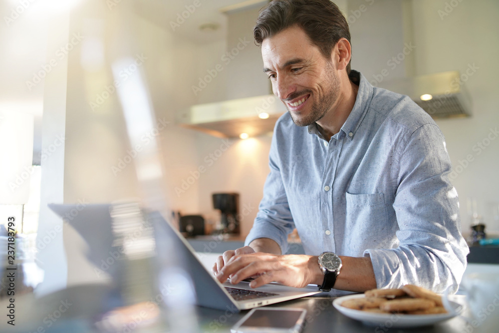 Handsome man with computer in modern kitchen Handsome man with computer in modern kitchen