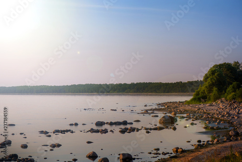 Beautiful sunset or sunrise landscape over rocky beach, seashore with big stones. Couple is sitting and relaxing. Kid jumping over rocks. Concept of relaxing family holidays, camping in nature. 