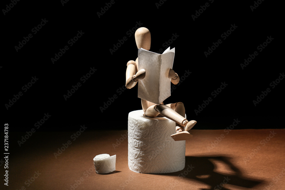 Small wooden mannequin reading newspaper while sitting on toilet paper