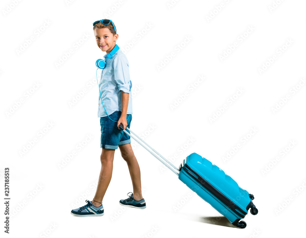 Full body of Boy with sunglasses and headphones traveling with his suitcase on isolated white background Full body of Boy with sunglasses and headphones traveling with his suitcase on isolated white background