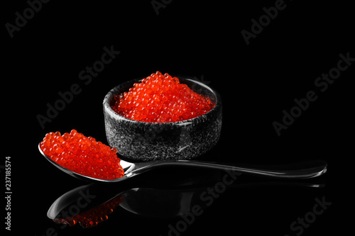 Bowl and spoon with delicious red caviar on dark background photo