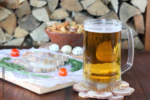 Mug of light beer and snack on the table against the background of firewood.