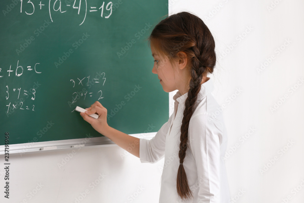 Cute girl writing on chalkboard in classroom Cute girl writing on chalkboard in classroom