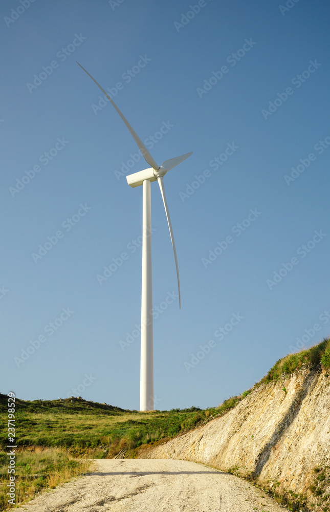 Wind turbine on hill generating electricity over a blue sky background. Clean and ecological energy production concept. Wind turbine on hill generating electricity over a blue sky background. Clean and ecological energy production concept.