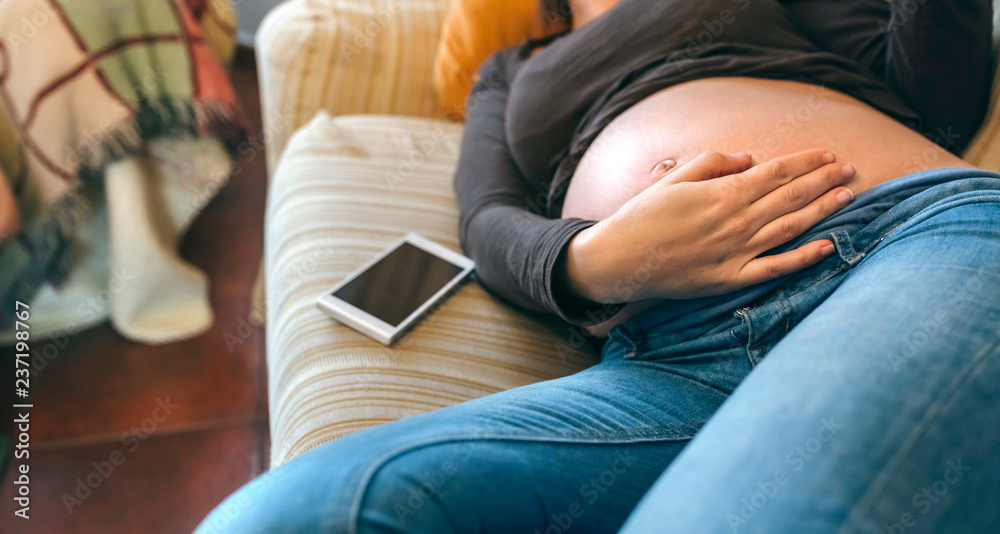Pregnant woman lying on the couch caressing her belly in the living room