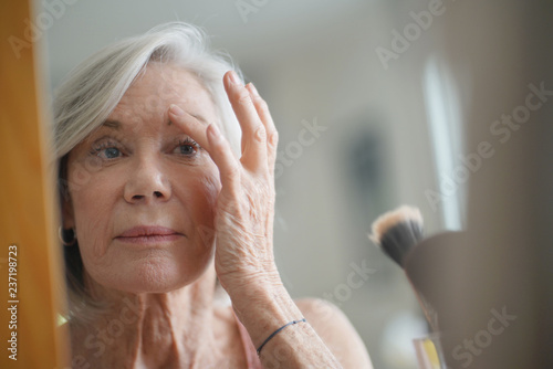 Attractive senior woman looking at her skin in the mirror