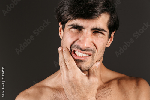 Displeased young man with toothache posing isolated over dark wall background.