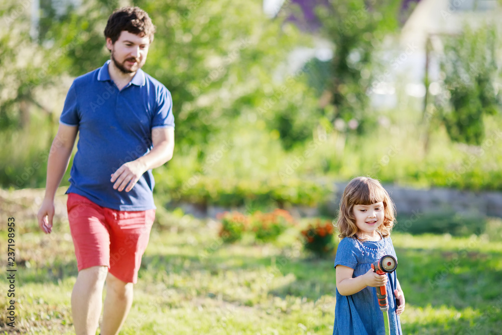 Father and daughter having fun in the garden, watering plants Father and daughter having fun in the garden, watering plants
