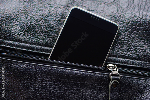 Black smart phone looks out from the unzipped leather pocket. Zipper and cell phone close-up with a place for the copy space.