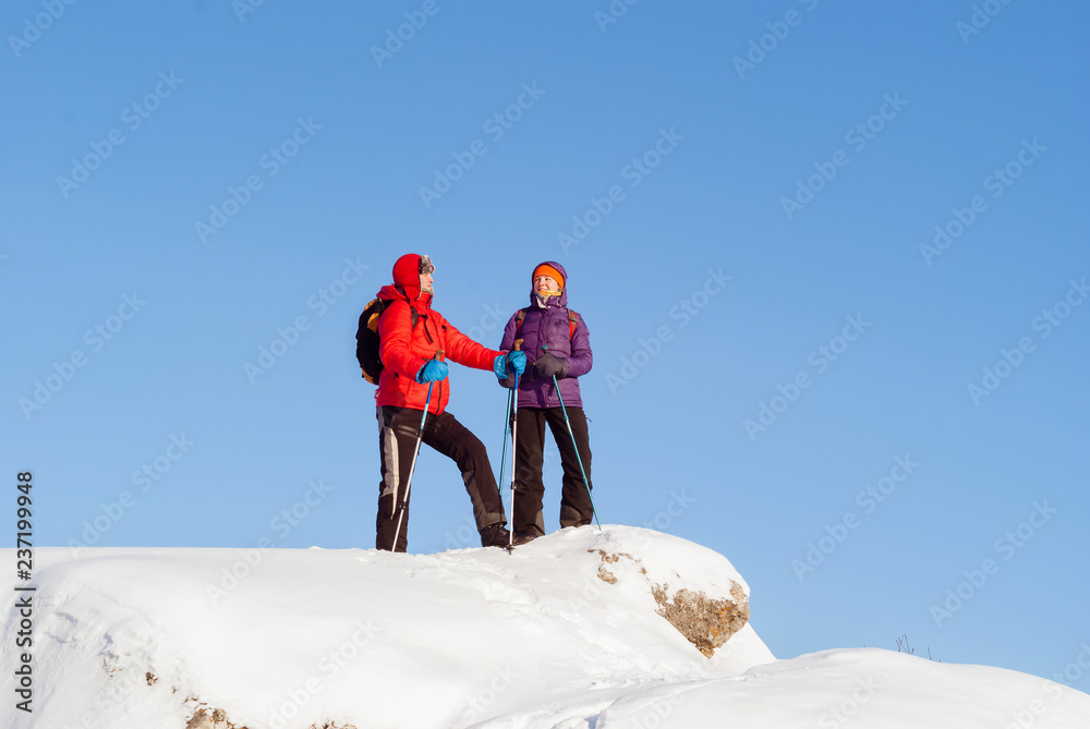 man and woman hikers on the top of a snowy hill on a frosty winter day against the sky..