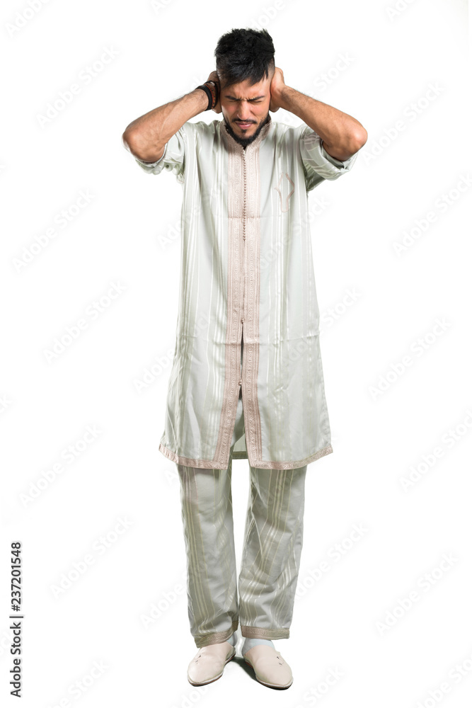 A full-length shot of a Arabic young man wearing typical arab clothes covering both ears with hands on isolated white background A full-length shot of a Arabic young man wearing typical arab clothes covering both ears with hands on isolated white background
