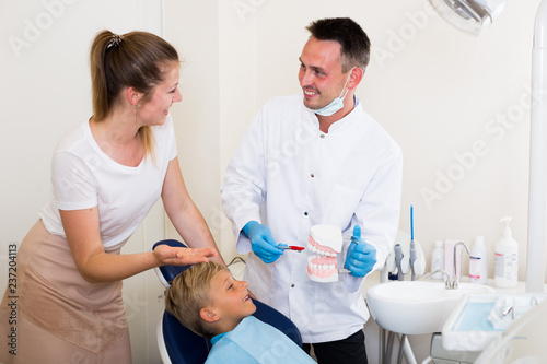 Dental in white is telling to young boy and mother about healthcare