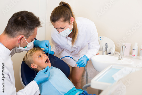 Male dentist is diagnosing the child while assistant is writing down patient's complaint