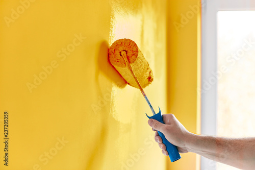 Male hand painting wall with paint roller. Painting apartment, renovating with sunflower color paint photo