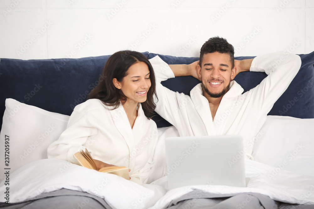 Young couple with laptop and book resting in bed Young couple with laptop and book resting in bed