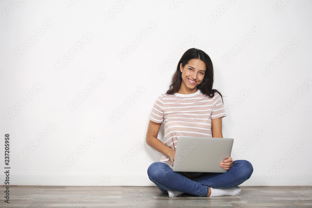 Young woman with laptop sitting on floor near light wall Young woman with laptop sitting on floor near light wall
