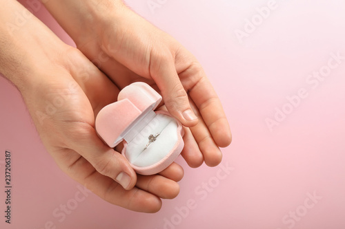 Male hands holding box with engagement ring on color background