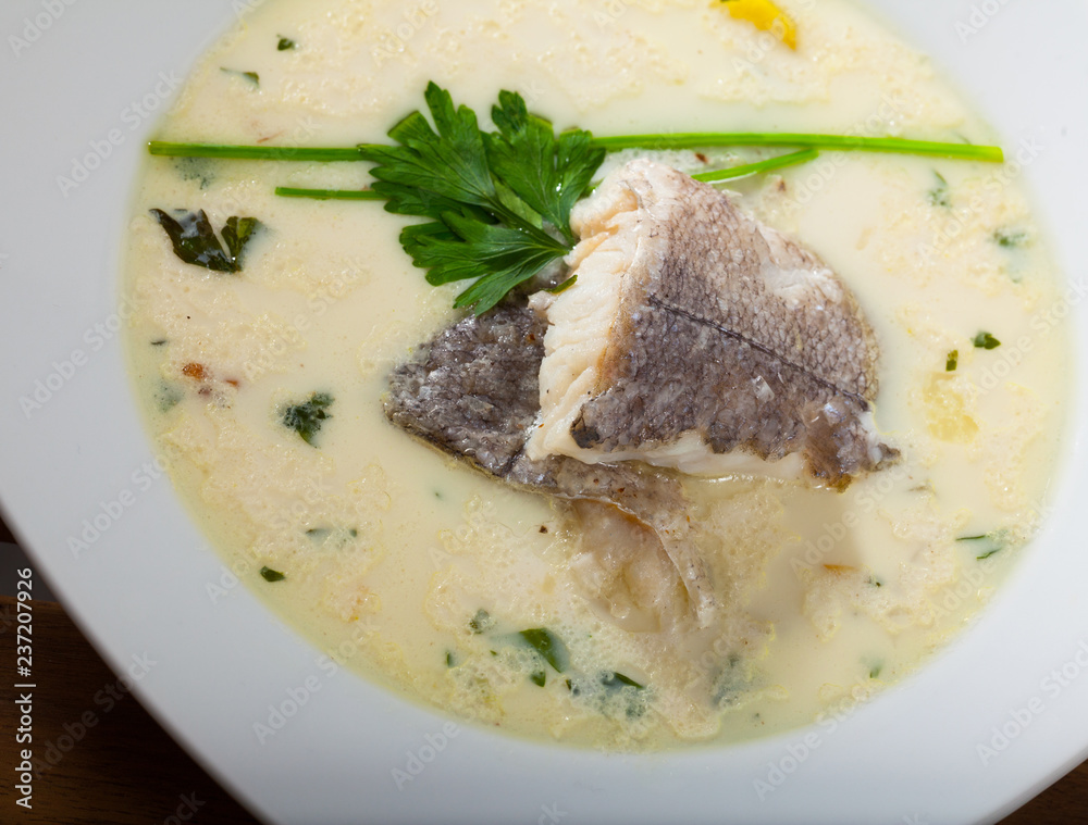 Tasty creamy soup with white fish hake and greens at plate