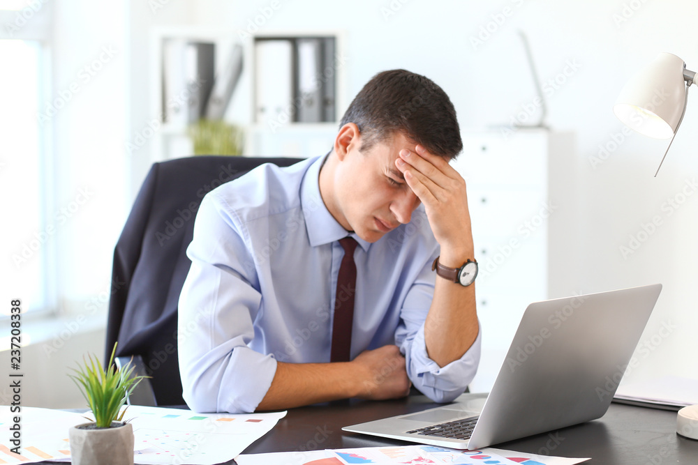 Young businessman suffering from headache in office Young businessman suffering from headache in office