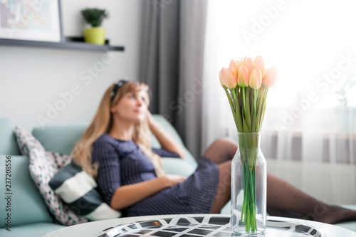 Fresh pinkl tulips on table at home, young woman relaxing on sofa in blurred background photo