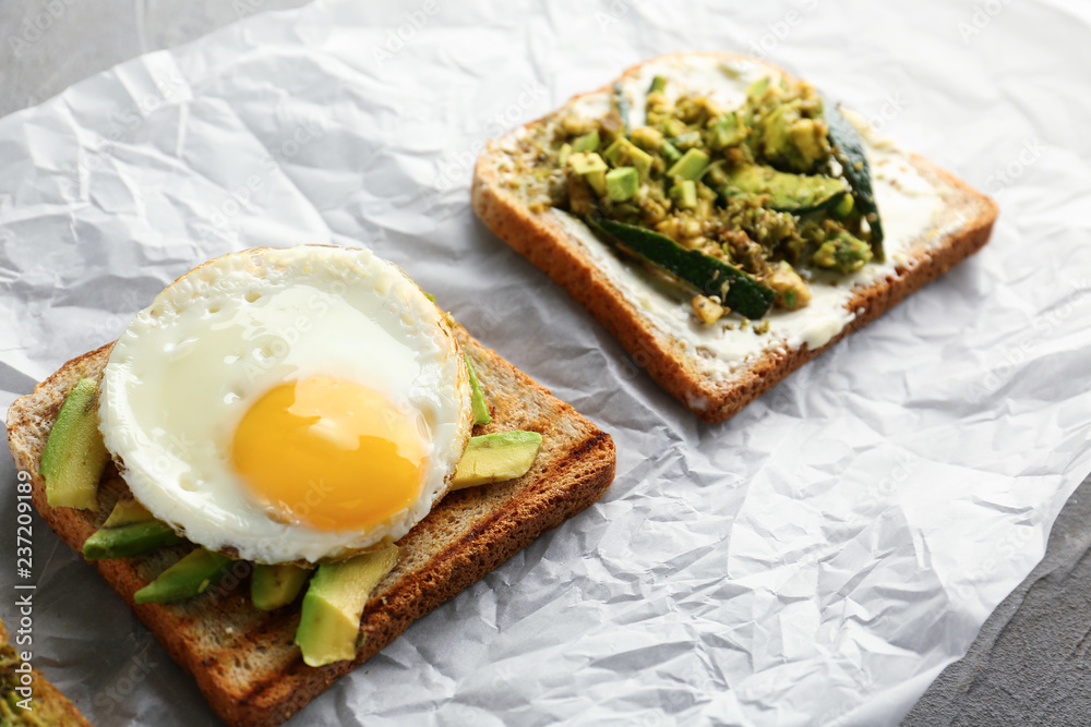 Tasty toasted bread with avocado and fried egg on parchment Tasty toasted bread with avocado and fried egg on parchment