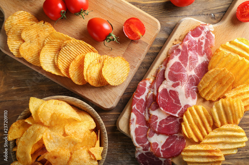 Tasty crispy potato chips with bacon and tomatoes on wooden table photo