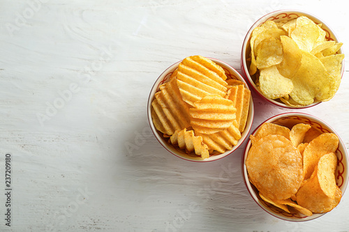 Bowls with tasty crispy potato chips on white wooden table