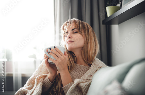 Fotografie, Obraz Happy woman in soft sweater relaxing at home with cup of hot tea or coffee